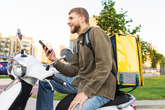 Il lavoro di un corriere su uno scooter in una grande città Un uomo con un telefono guarda l'indirizzo di consegna