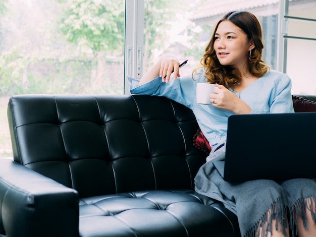 Il lavoro online della donna abbastanza asiatica online a casa e si rilassa lo stile di vita con il suo labtop