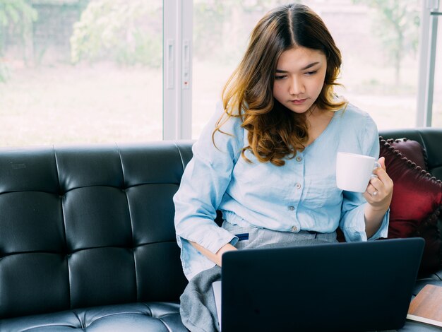 Il lavoro online della donna abbastanza asiatica online a casa e si rilassa lo stile di vita con il suo labtop