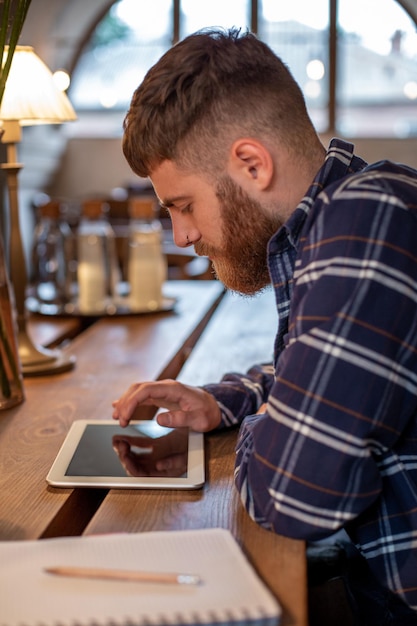 Il libero professionista vestito con abiti casual si concentra sulla lettura di notizie e sulla visualizzazione su tablet digitale mentre è seduto...