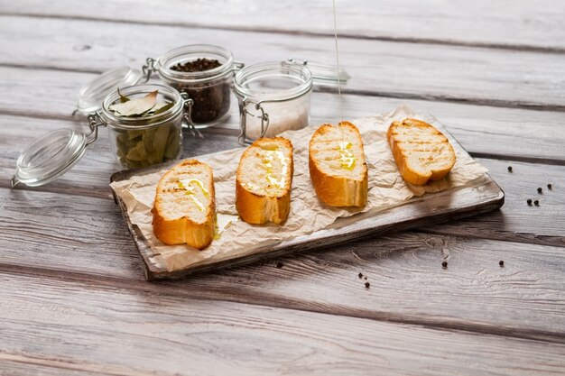 Il liquido si versa sulla fetta di baguette. Vaso con pepe intero. Come preparare la merenda italiana. Pane grigliato e olio d'oliva.