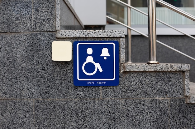 Il logo blu delle persone con disabilità accanto al pulsante per chiedere aiuto e il testo in braille