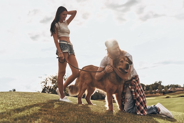 Il loro migliore amico. Bel giovane che abbraccia il suo cane mentre trascorre il tempo libero con la sua ragazza nel parco