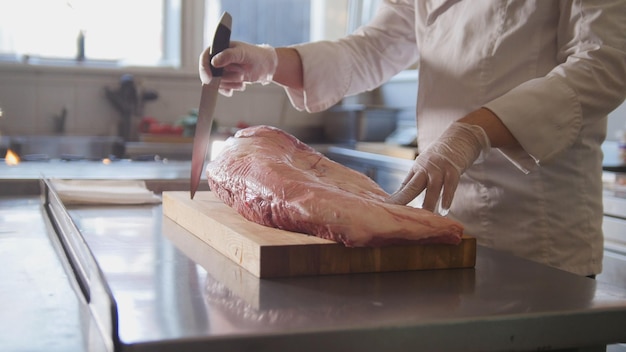 Il macellaio prepara un grande pezzo di carne fresca cruda che giace su una tavola di legno in una cucina commerciale, cucina e concetto di alta cucina