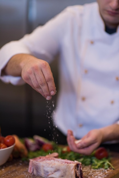 Il maestro chef mette sale su una succosa fetta di bistecca cruda con verdure su un tavolo di legno