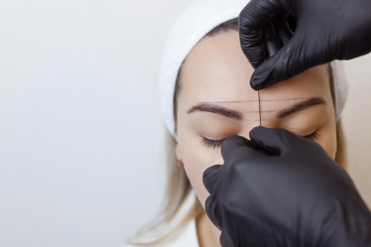 Il maestro del trucco permanente del sopracciglio del tatuaggio del sopracciglio applica il contorno con il filo sui clienti