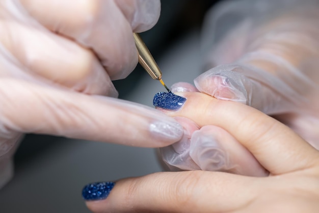 Il maestro della manicure applica lo strato finale di smalto gel sull'unghia della cliente