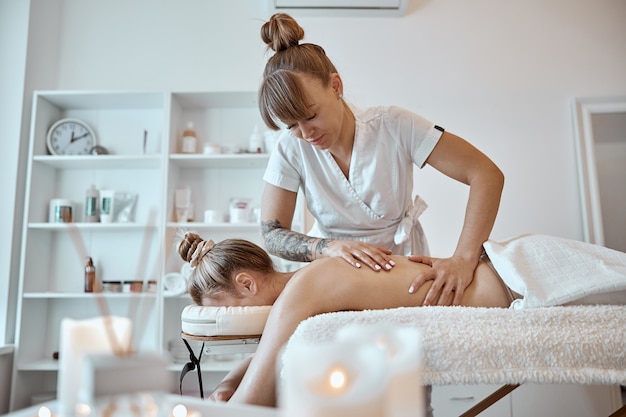 Il maestro di massaggi professionale e sicuro sta eseguendo procedure per una donna caucasica in un moderno minimalista