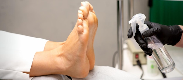 Il maestro di pedicure disinfetta i piedi della donna con la decontaminazione della preparazione nel salone di bellezza.