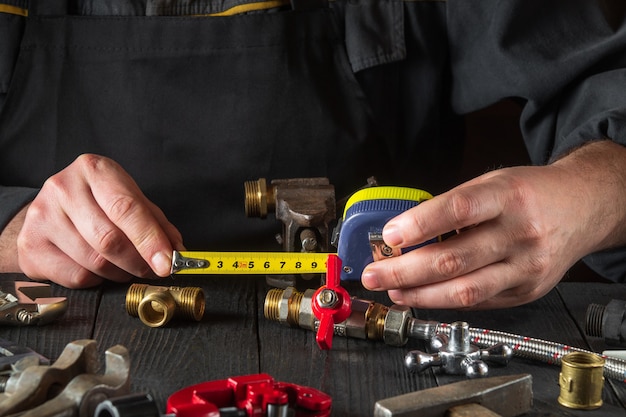Il maestro idraulico misura la distanza usando un metro a nastro. Ambiente di lavoro in officina con attrezzi e pezzi di ricambio sul tavolo