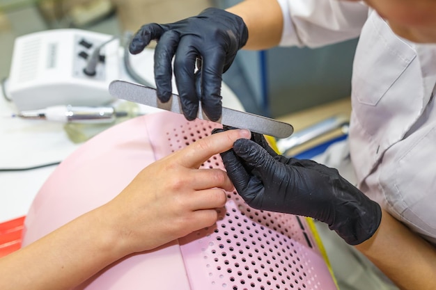 Il maestro in guanti neri nel salone fa manicure pedicure al cliente