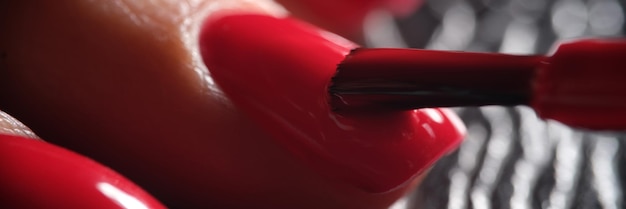 Il maestro manicure applica una vernice rossa brillante decorativa sulla lamina ungueale con il pennello