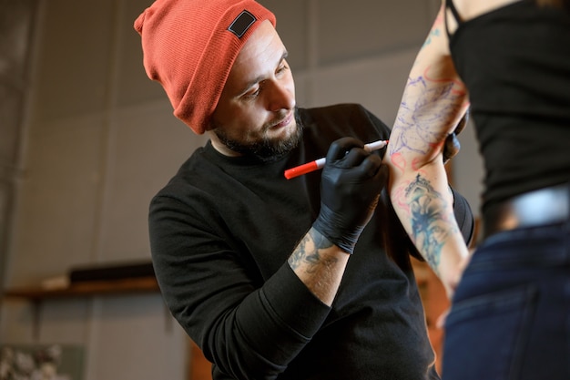 Il maestro professionista del tatuaggio caucasico barbuto maschio sta lavorando in un accogliente studio atmosferico