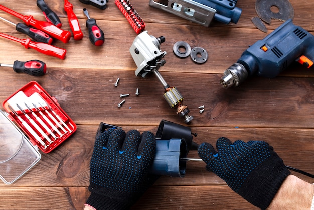 Il maestro ripara un dispositivo elettrico rotto: trapano, taglierina su un tavolo di legno. Officina riparazioni utensili elettrici