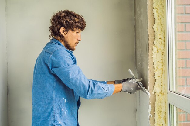 Il maestro sta applicando stucco bianco su un muro e spalma con una spatola in una stanza di ristrutturazione della casa durante il giorno