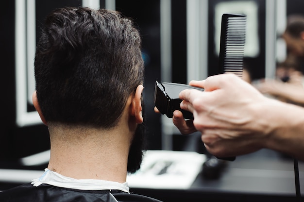 Il maestro taglia i capelli e la barba degli uomini nel barbiere, il parrucchiere fa acconciatura per un giovane