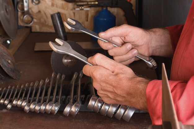 Il maestro tiene in mano due chiavi di un mazzo di chiavi su un banco di lavoro con attrezzi in garage