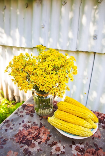 Il mais bollito si trova su un piatto sul tavolo insieme a un bouquet di fiori gialli Soleggiata giornata estiva