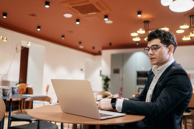 Il manager con gli occhiali lavora in ufficio utilizza un computer portatile e fa un rapporto online