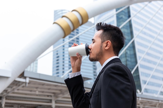 Il manager felice dell'uomo d'affari di successo beve il caffè in una tazza di carta al mattino al centro del moderno ufficio affari nel centro cittadino
