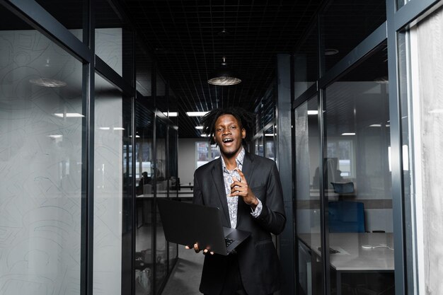 Il manager nero allegro di affari con il computer portatile sta puntando il dito verso l'alto e sta sorridendo in ufficio.