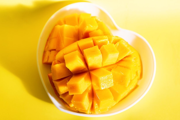 Il mango splendidamente affettato giace su un piatto a forma di cuore su uno sfondo giallo. Frutti tropicali. Vista dall'alto