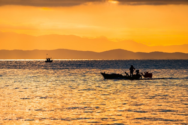 Il mare della Thailandia al crepuscolo con la nave Silhouette e il pescatore in mare