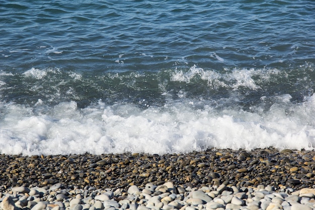 Il mare spumeggiante ondeggia su una spiaggia di ciottoli deserta in estate