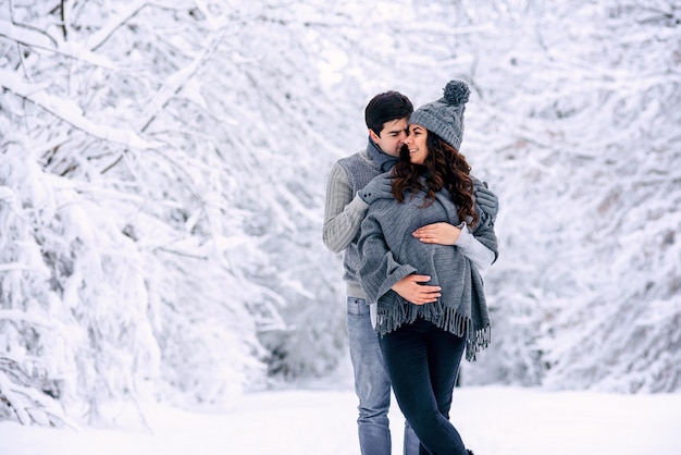 Il marito abbraccia teneramente la sua bella moglie incinta in un parco invernale innevato