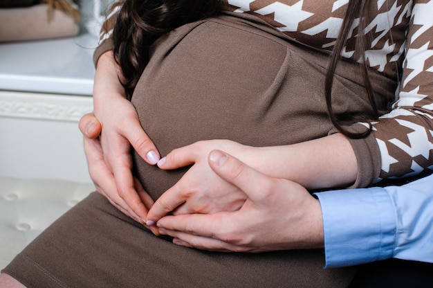 Il marito attento abbraccia teneramente la moglie incinta e le sue mani giacciono sul suo ventre a forma di cuore