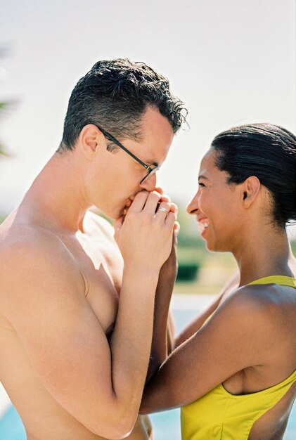 Il marito bacia le mani della moglie sorridente mentre è in piedi vicino alla piscina