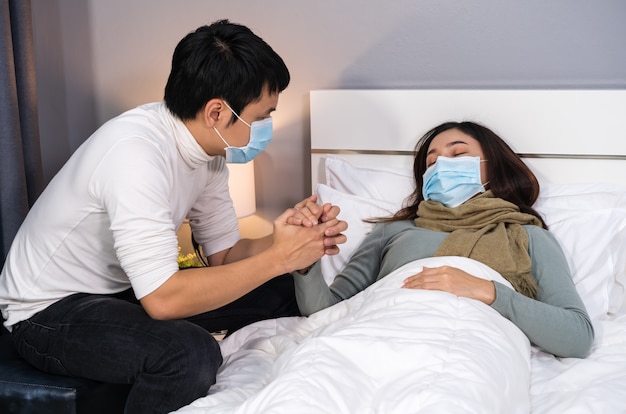 Il marito preoccupato si prende cura della moglie malata mentre dorme sul letto di casa, le persone devono indossare una maschera medica che protegge dalla pandemia di coronavirus