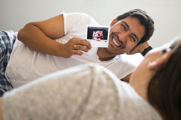 Il marito sorride mentre mostra l'immagine ecografica del suo nuovo bambino a letto con sua moglie