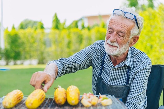 Il maschio anziano sano dell'uomo anziano si rilassa lo stile di vita cucinando cibo griglia mais cortile all'aperto