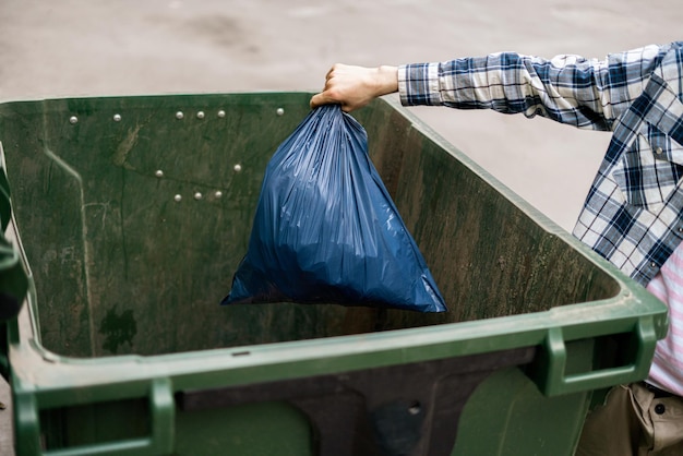 Il maschio scarica il pacchetto di rifiuti in un grande contenitore per rifiuti