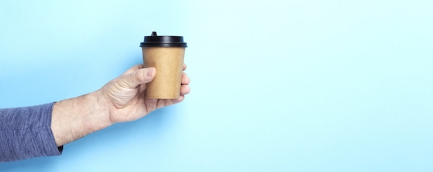 Il maschio tiene la tazza di carta della mano con caffè su fondo blu. Copia spazio