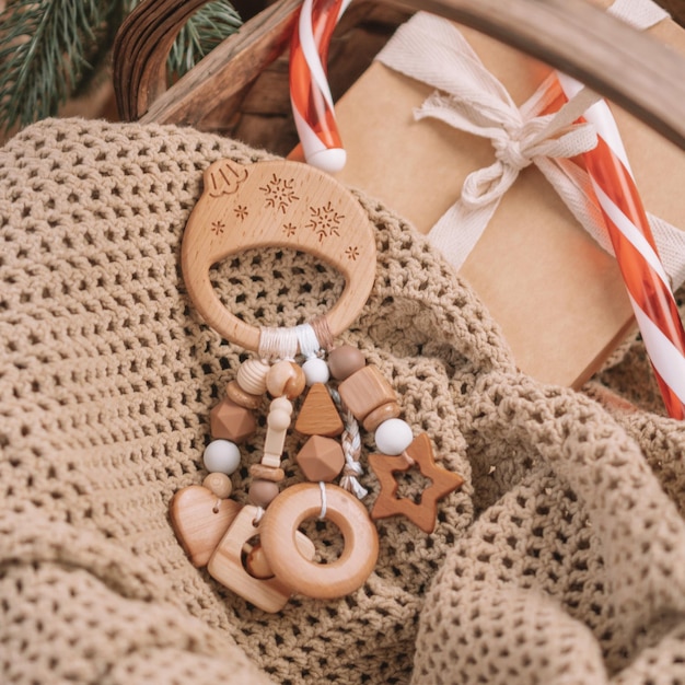 Il massaggiagengive per bambini a forma di palla di Natale in legno con perline di silicone si trova tra i regali su una coperta nel cesto sotto l'albero di Natale. Uso di instagram con cornice quadrata