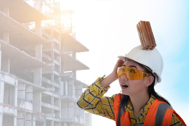 Il mattone del blocco di bastone è caduto sulla testa della giovane donna dell'ingegnere asiatico sul lavoratore del casco