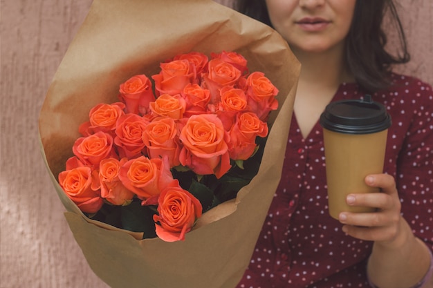 Il mazzo della tenuta della donna delle rose e una tazza di carta di portano via la bevanda