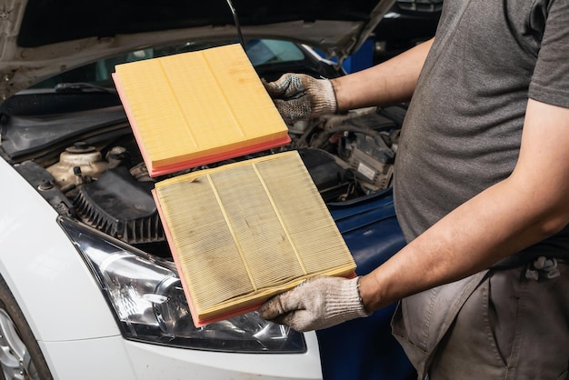 Il meccanico auto mostra il filtro dell'aria del motore vecchio e nuovo per un'auto passeggeri