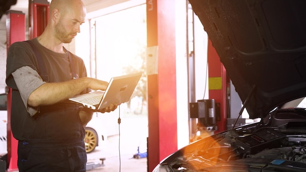 Il meccanico automatico diagnostica un'auto utilizzando un primo piano dell'officina dell'auto del computer