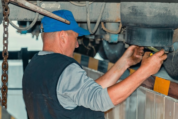 Il meccanico automobilistico si trova nella fossa di ispezione del servizio di auto e ripara il camion Il vero fabbro risolve i problemi sul camion