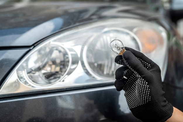 Il meccanico cambia la lampadina anabbagliante o abbagliante nella sua auto, primo piano