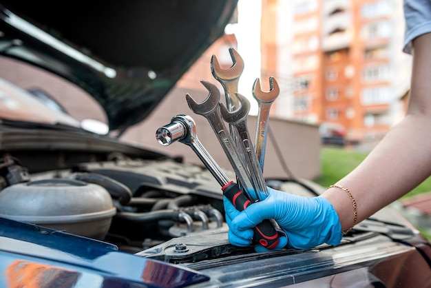 Il meccanico dell'auto ripara il motore di un'auto vicino a un'auto con il cofano aperto