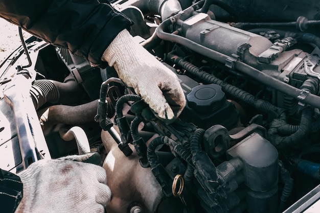 Il meccanico di auto ripara il motore di un'auto Mans mani in guanti da lavoro primo piano Diagnostica e ripristino di vecchie parti Sostituzione di cavi ad alta tensione