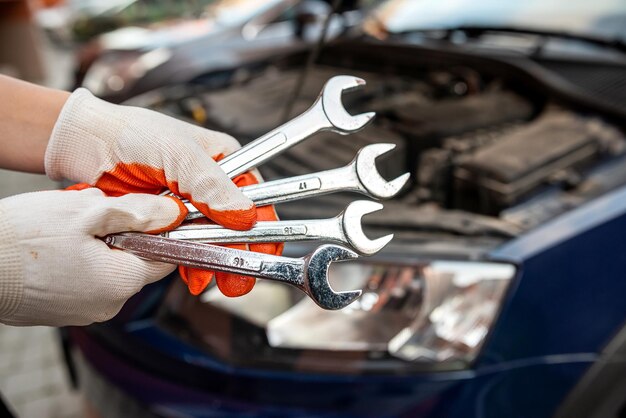 Il meccanico di automobili ripara un motore di un'auto vicino a un'auto con servizi di riparazione di manutenzione di auto con cofano aperto