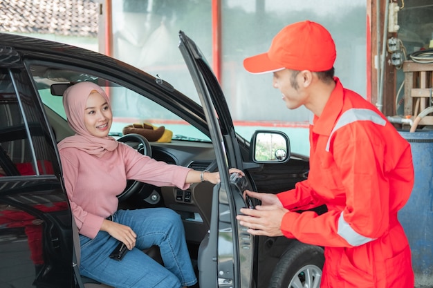 Il meccanico in divisa rossa apre la portiera dell'auto quando il cliente si presenta all'auto per essere riparata in officina