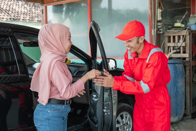 Il meccanico in rosso riceve le chiavi dell'auto quando il cliente arriva in auto per essere riparato in officina