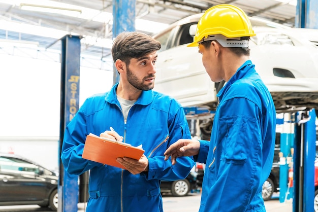 Il meccanico in uniforme blu da lavoro controlla la lista di controllo della manutenzione del veicolo con il suo assistente