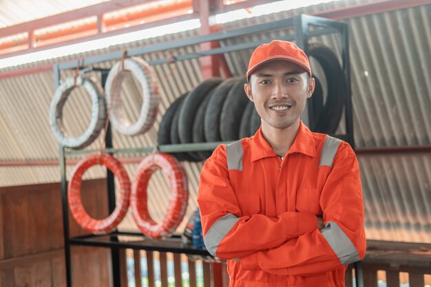 Il meccanico in uniforme da wearpack con le mani incrociate sta con il portapneumatici